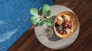 Mesa redonda com uma tigela de comida, um copo de vinho e um vaso de planta perto de uma piscina.