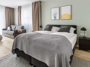 A modern bedroom with a large bed, grey and white bedding, a grey sofa, and two framed pictures on the wall. - Limehome Osnabrück Johannisstraße (Osnabrueck)