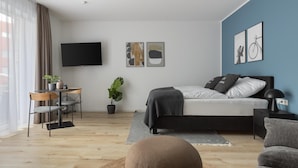 A modern bedroom with a bed, bedside table, lamp, and a TV on the wall. - Limehome Osnabrück Johannisstraße (Osnabrueck)