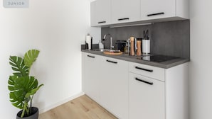 A modern kitchen with white cabinets, a black countertop, and a potted plant. - Limehome Osnabrück Johannisstraße (Osnabrueck)