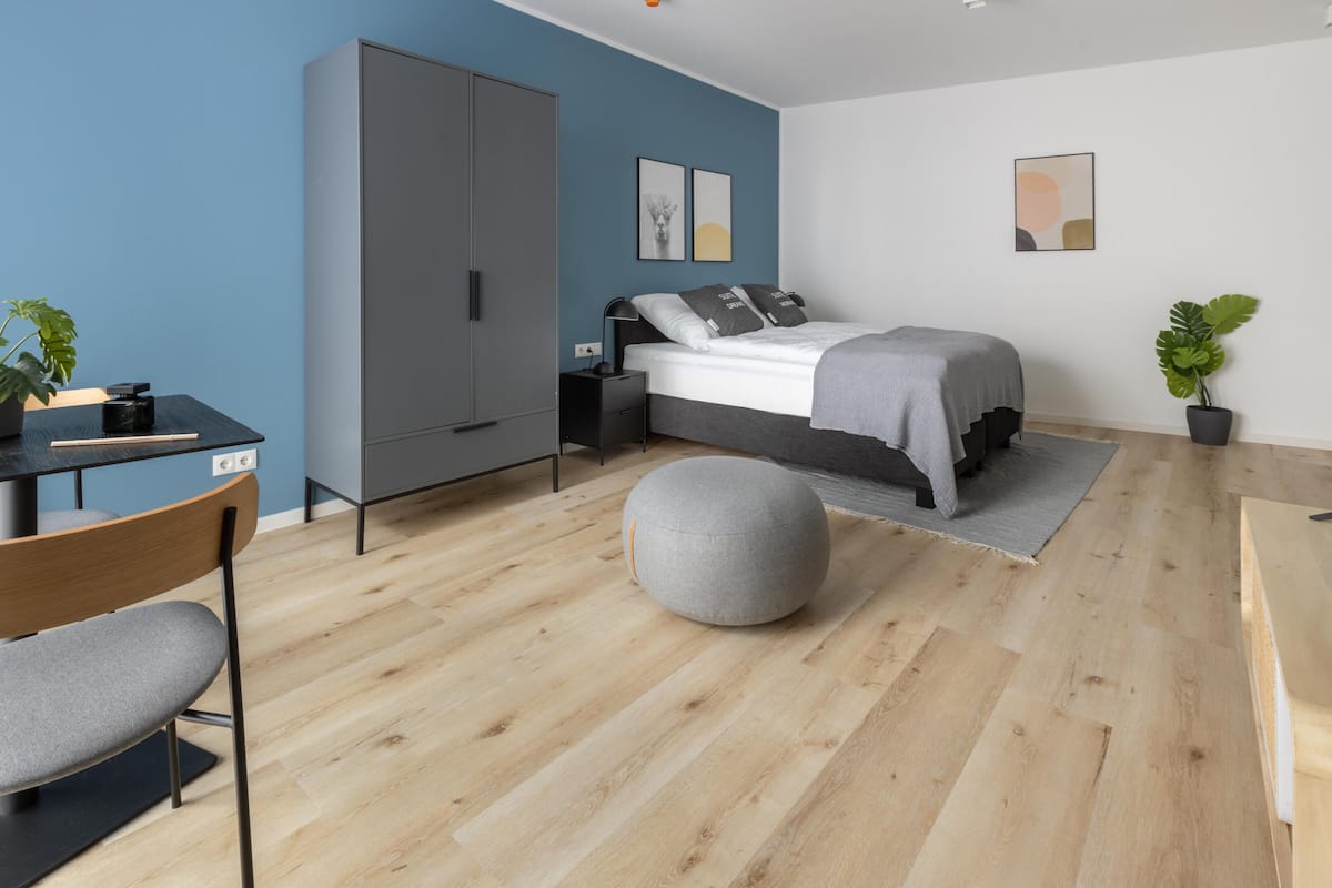 Ein modernes Schlafzimmer mit Bett, Nachttischen, einem Kleiderschrank, einem Schreibtisch mit Stuhl und einer Zimmerpflanze.
