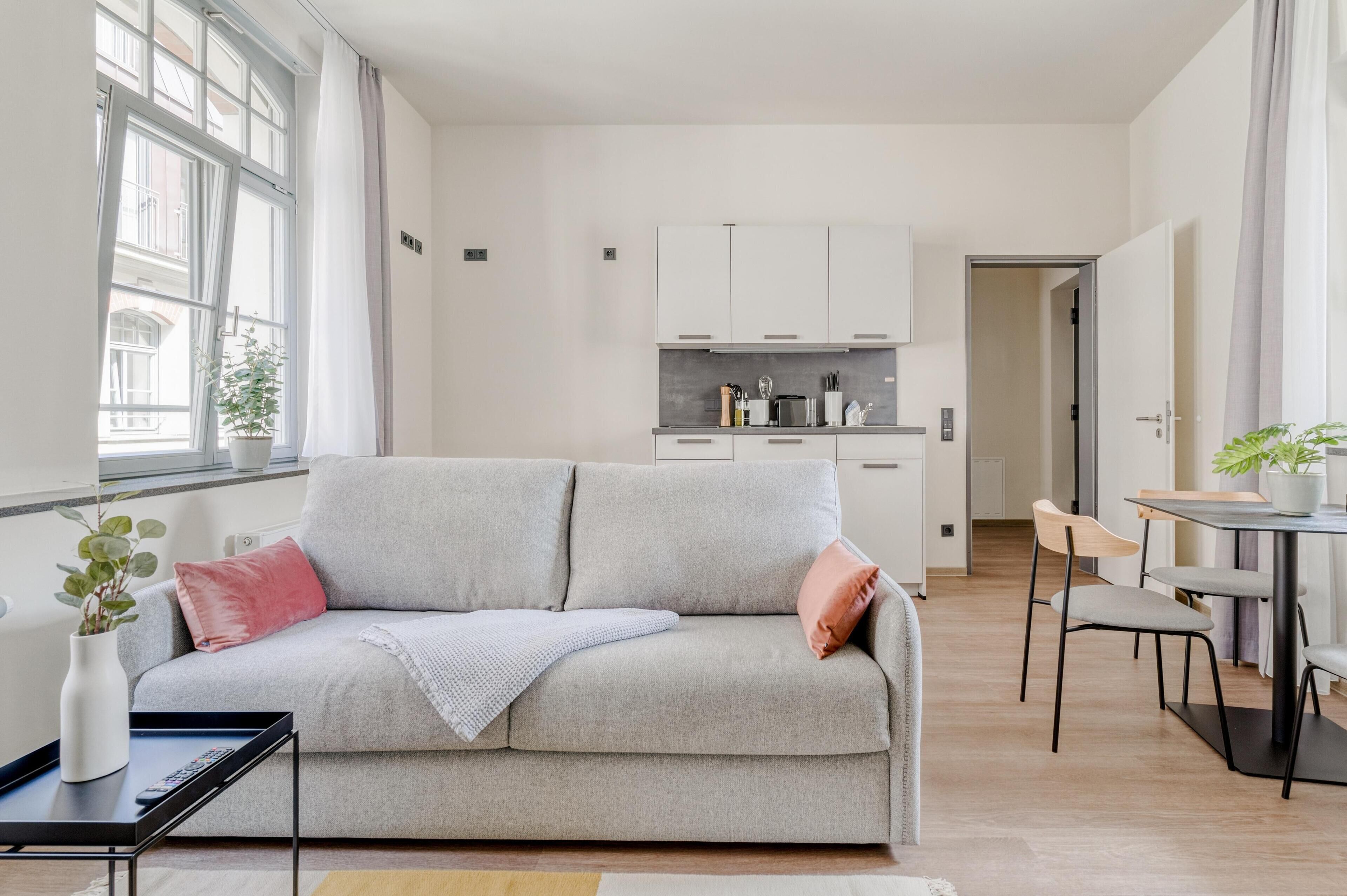 A modern living room with a sofa, a dining table, and a kitchen in the background.
