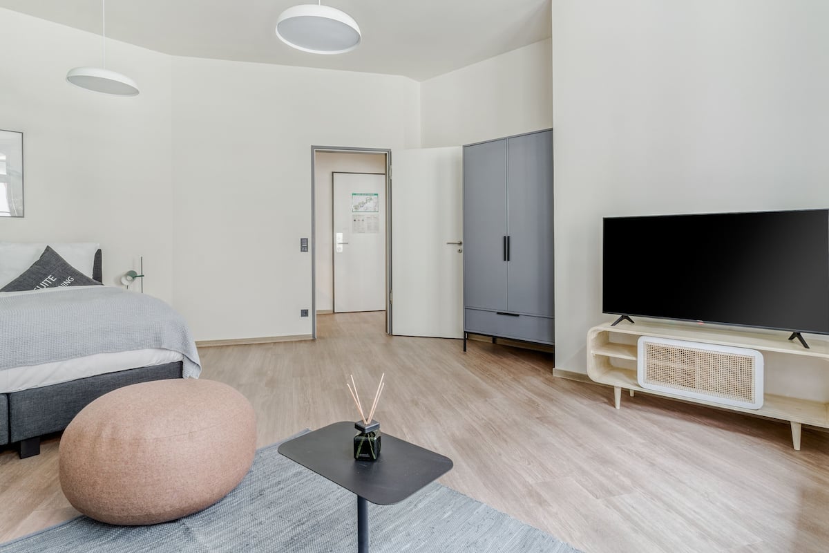 A modern hotel room with a bed, a television, a wardrobe, and a small table with a decorative item.