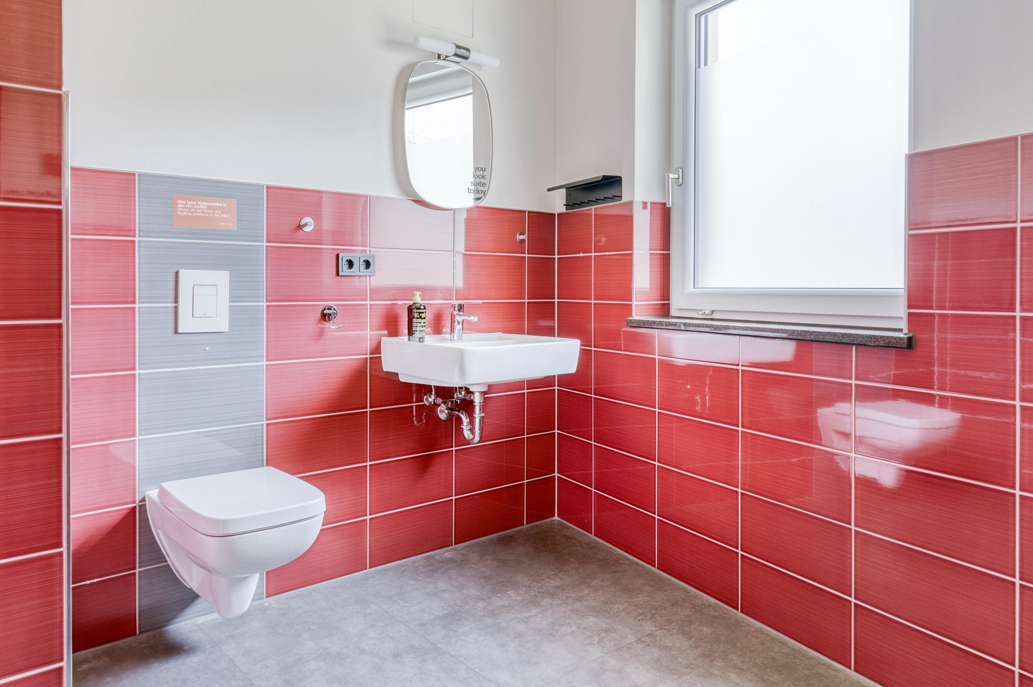 A bathroom with a white toilet, a white sink, and red tiled walls.
