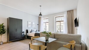 A modern living room with a sofa, two chairs, a table, a cabinet, and a potted plant. - Limehome Leipzig Oelßner's Hof (Leipzig)