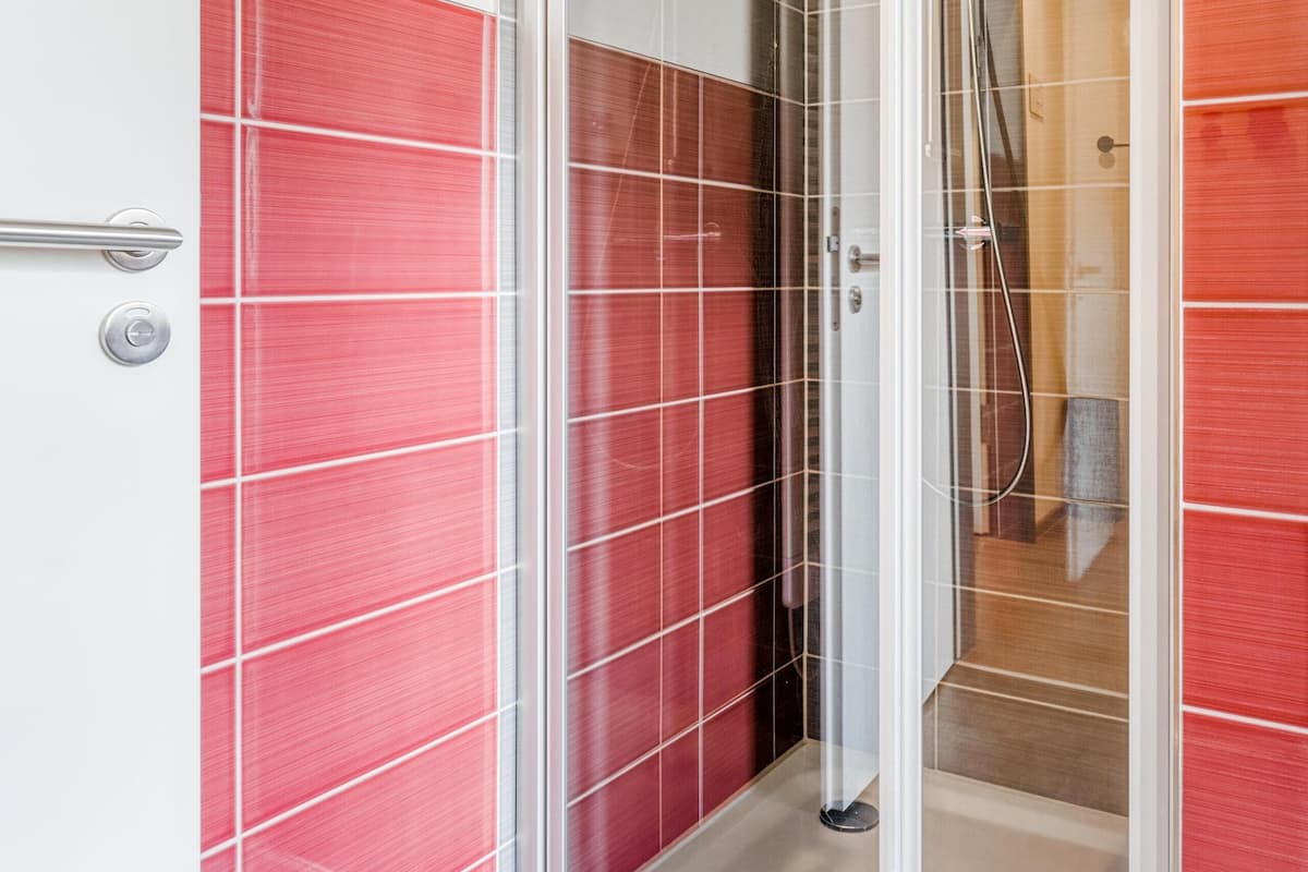 A shower area with a glass door, tiled walls in red and white, and a visible showerhead.