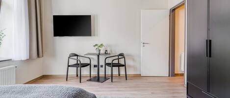 Un dormitorio moderno con cama, escritorio con dos sillas, televisor en la pared y armario.