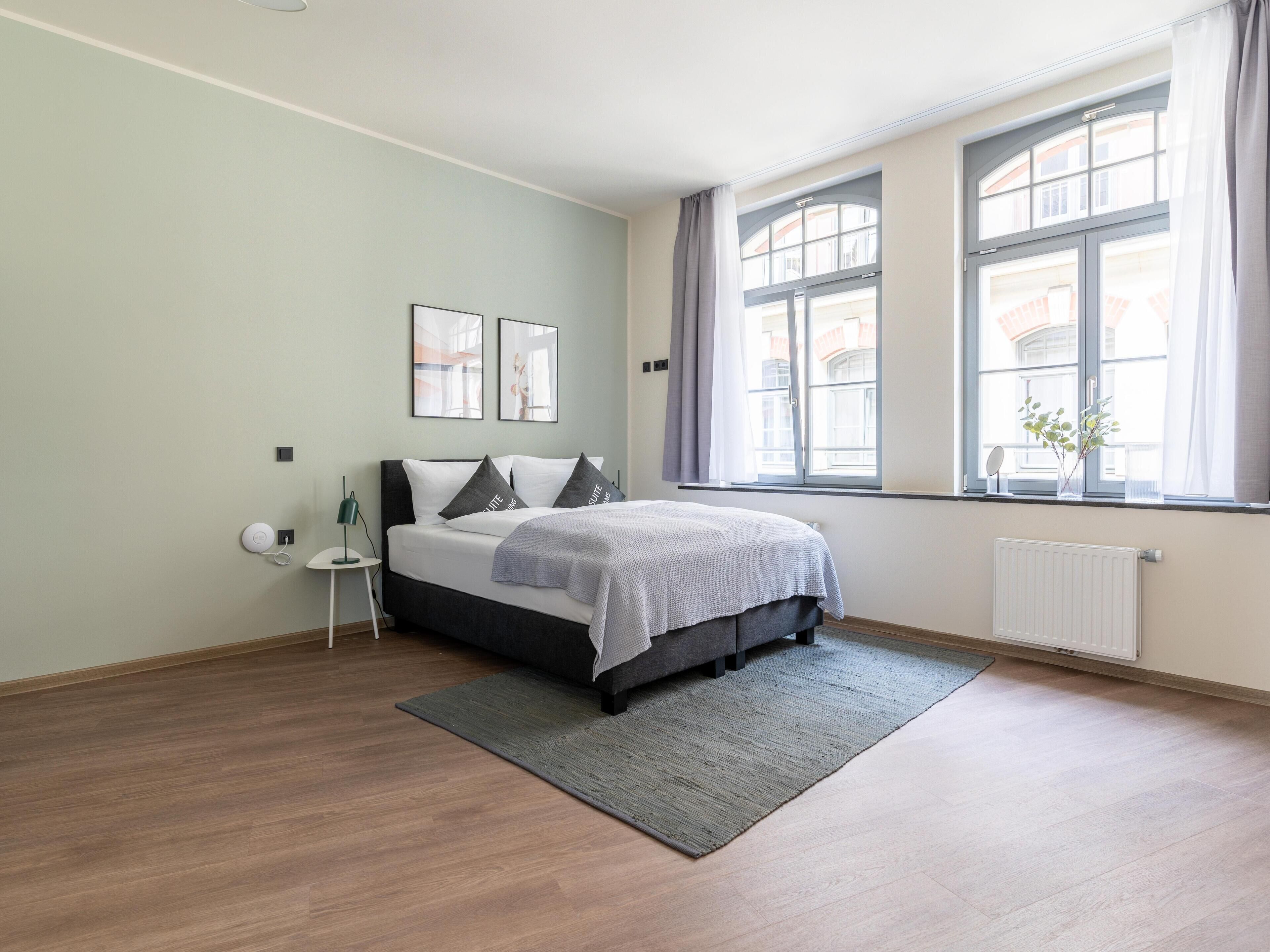 A modern bedroom with a large bed, a small bedside table, and a window with curtains.