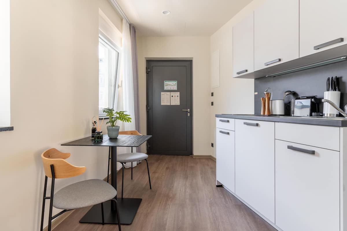 A compact kitchen with a dining area, featuring a table with chairs, a potted plant, and a dark door with a sign.