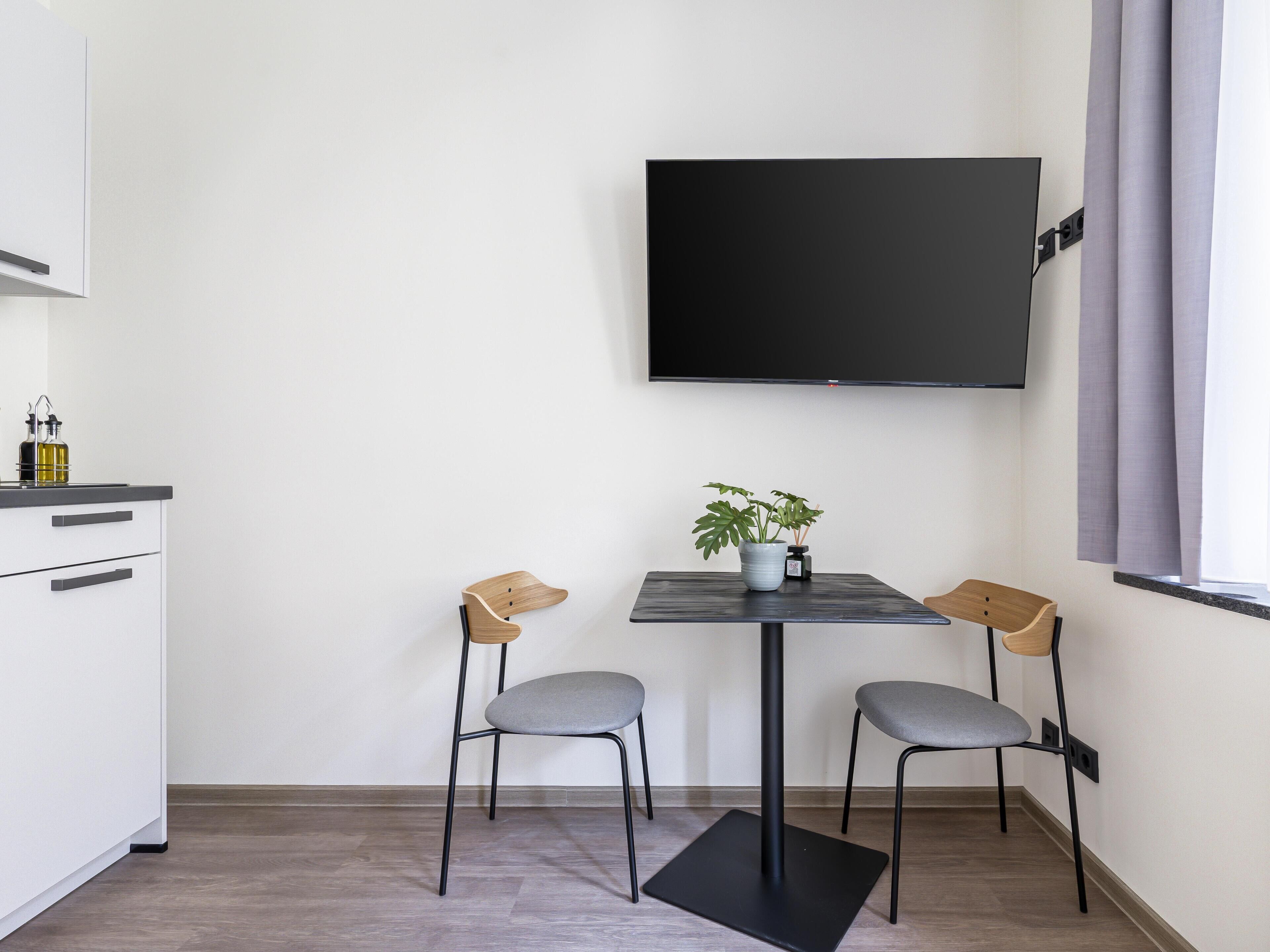 A small, modern kitchen with a white cabinet, a black countertop, and a single chair.