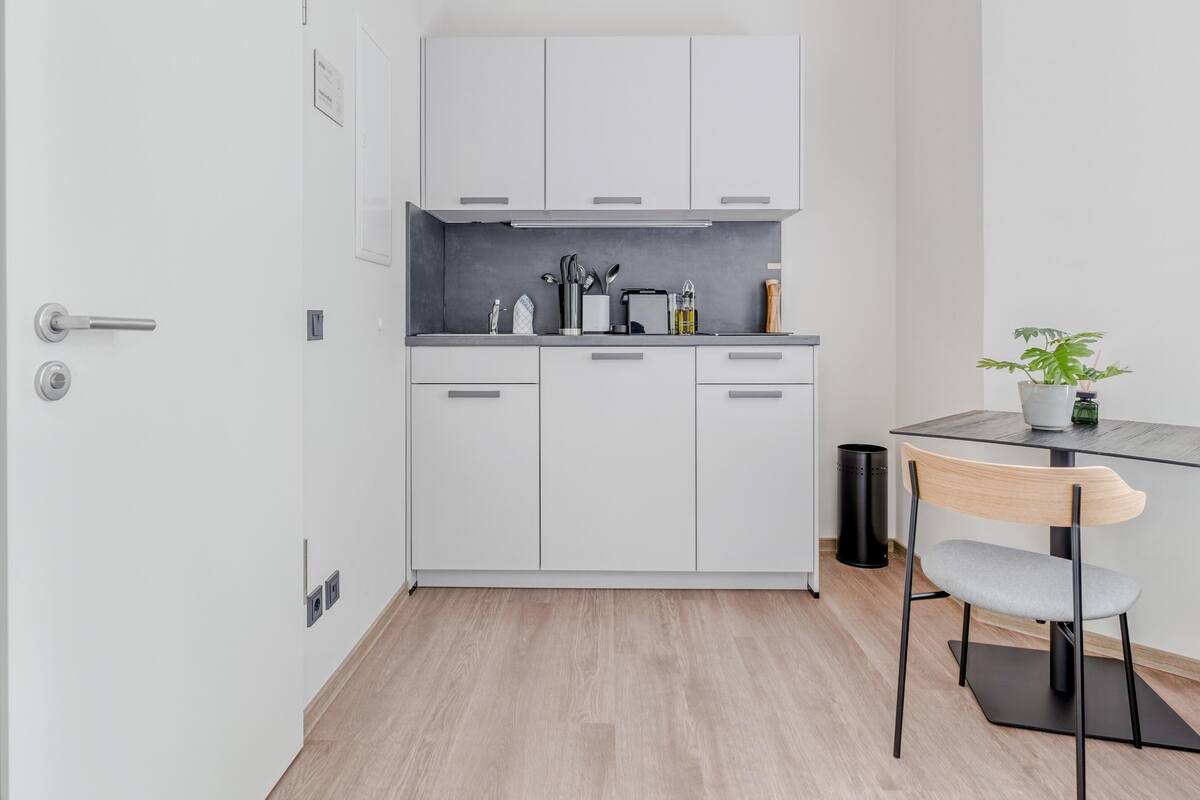 A modern kitchen with white cabinets, a black countertop, and a wooden chair.