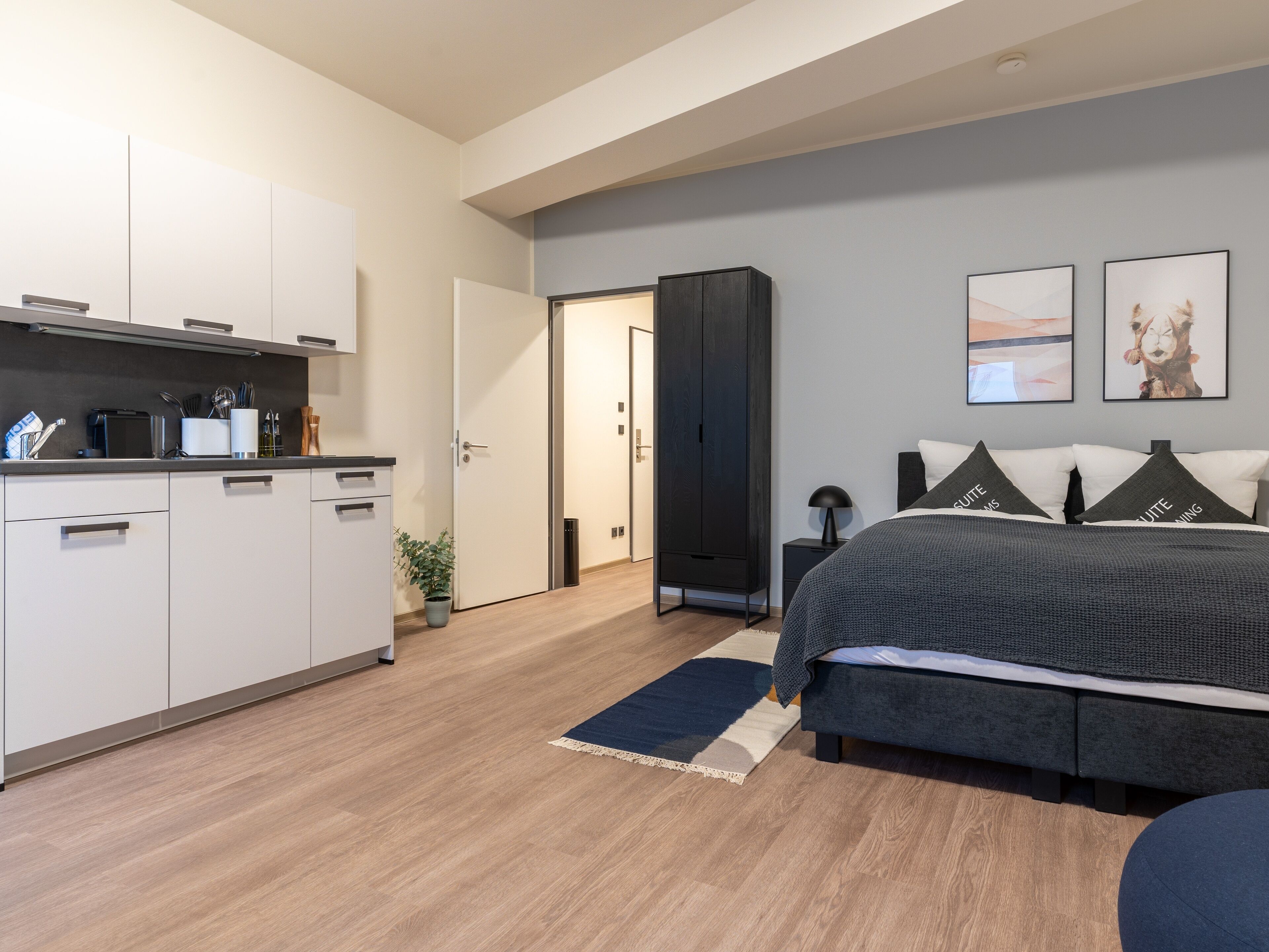 Un dormitorio moderno con cama, mesitas de noche, armario y una zona de cocina con armarios y electrodomésticos.