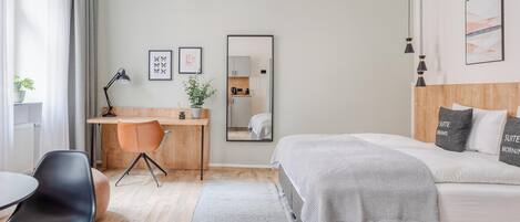 A modern hotel room with a bed, desk, chair, and a mirror.