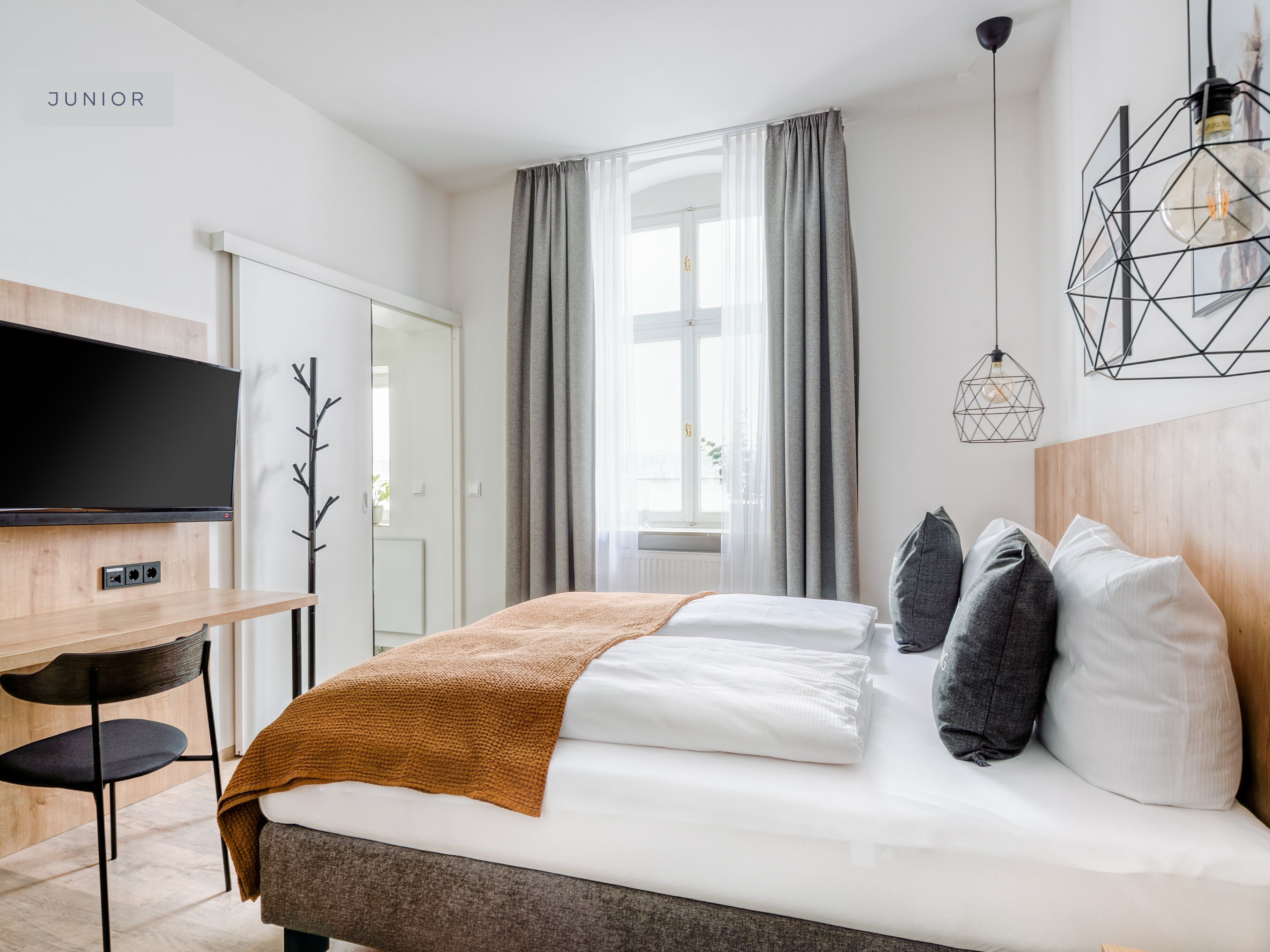 Un dormitorio moderno con cama, televisor montado en la pared y escritorio con silla.