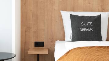 Ein modernes Schlafzimmer mit einem hölzernen Kopfteil, einem Nachttisch, einem gerahmten Bild an der Wand und einem Kissen mit dem Aufdruck 'SUITE DREAMS'.