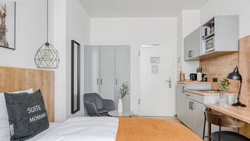 Una suite junior moderna con cama, una silla gris, una mesita, un escritorio y una kitchenette.