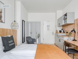 Una suite junior moderna con cama, una silla gris, una mesita, un escritorio y una kitchenette.