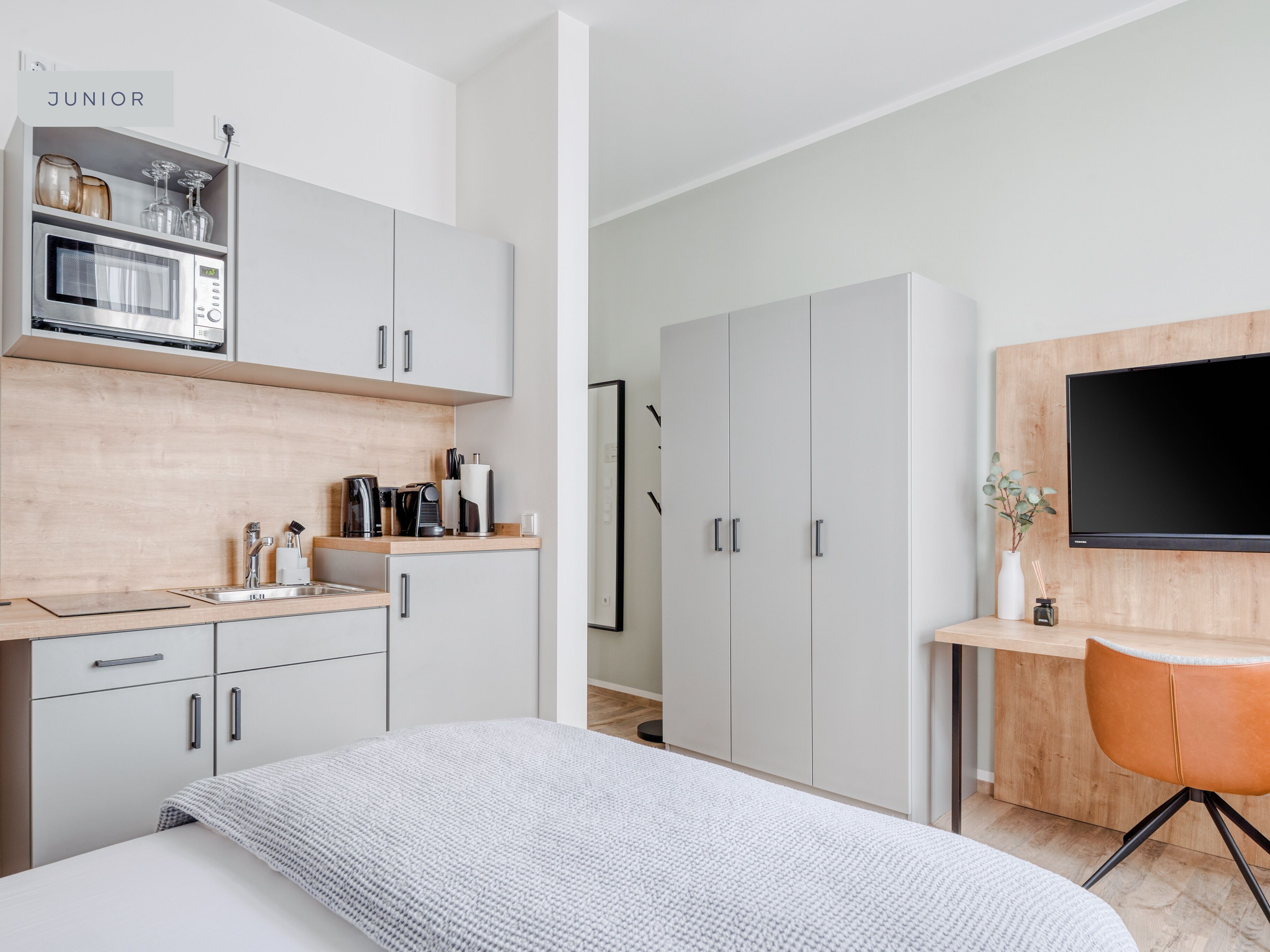 Un dormitorio moderno con cama, escritorio, televisor y armario.