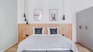 Une chambre moderne avec une tête de lit en bois, deux tables de chevet, une couvre-lit grise et deux lampes noires fixées au mur.