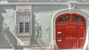 Fachada de edificio con puerta roja, una ventana con rejas y una placa con un número.