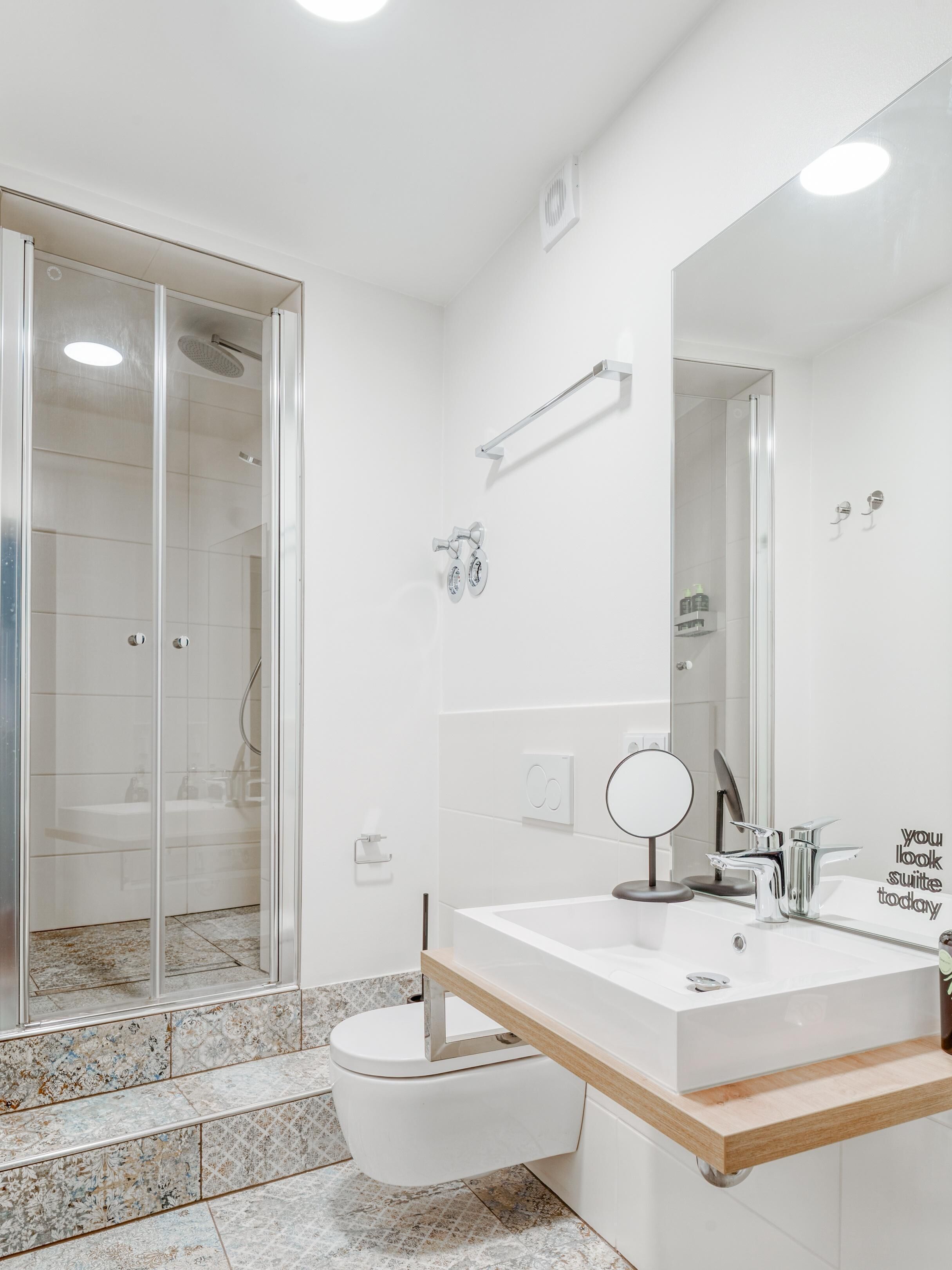Un baño moderno con cabina de ducha de vidrio, un lavabo blanco con espejo y un inodoro.