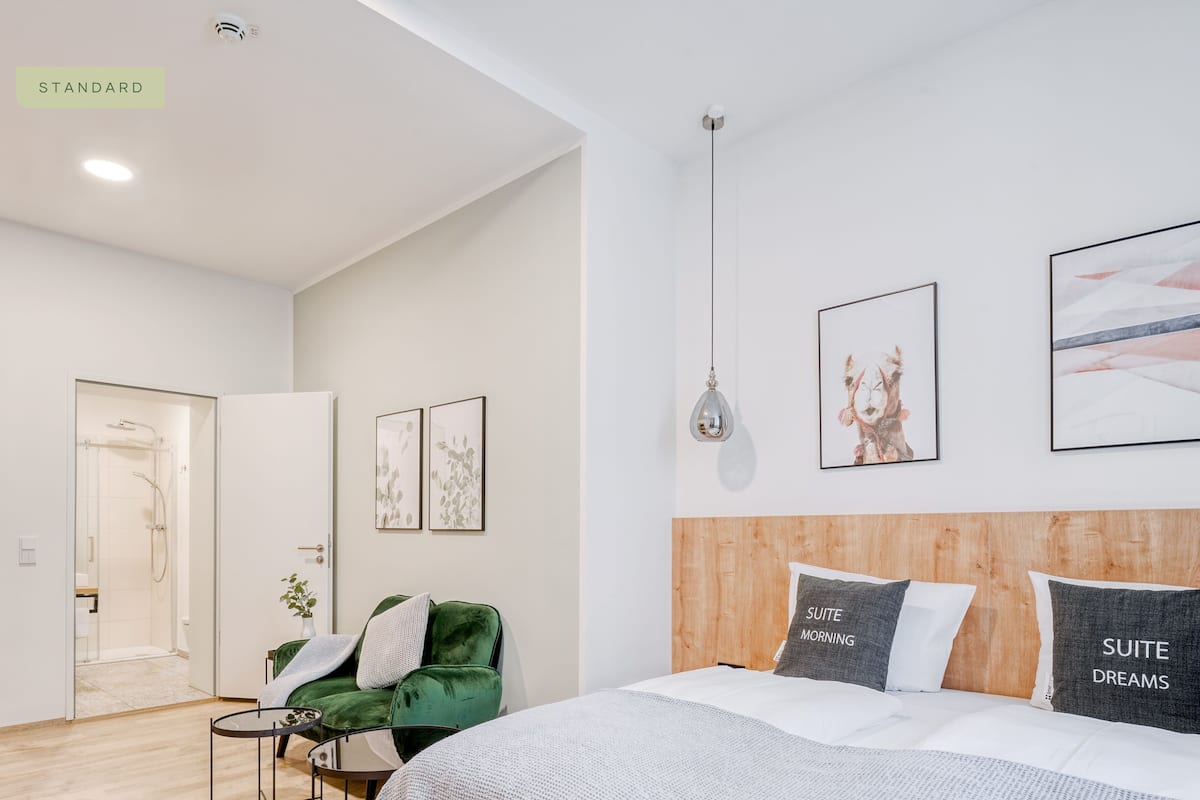 Een moderne slaapkamer met een groot bed, een groene fauteuil, een klein tafeltje en kunstwerken aan de wanden.