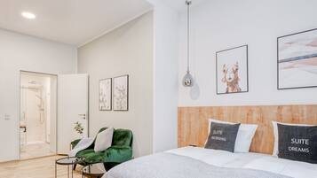 A modern bedroom with a large bed, a green armchair, a small table, and artwork on the walls.