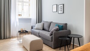 Una sala moderna con un sofá gris, una mesita auxiliar, una mesa de centro redonda y un ventanal con cortinas grises.