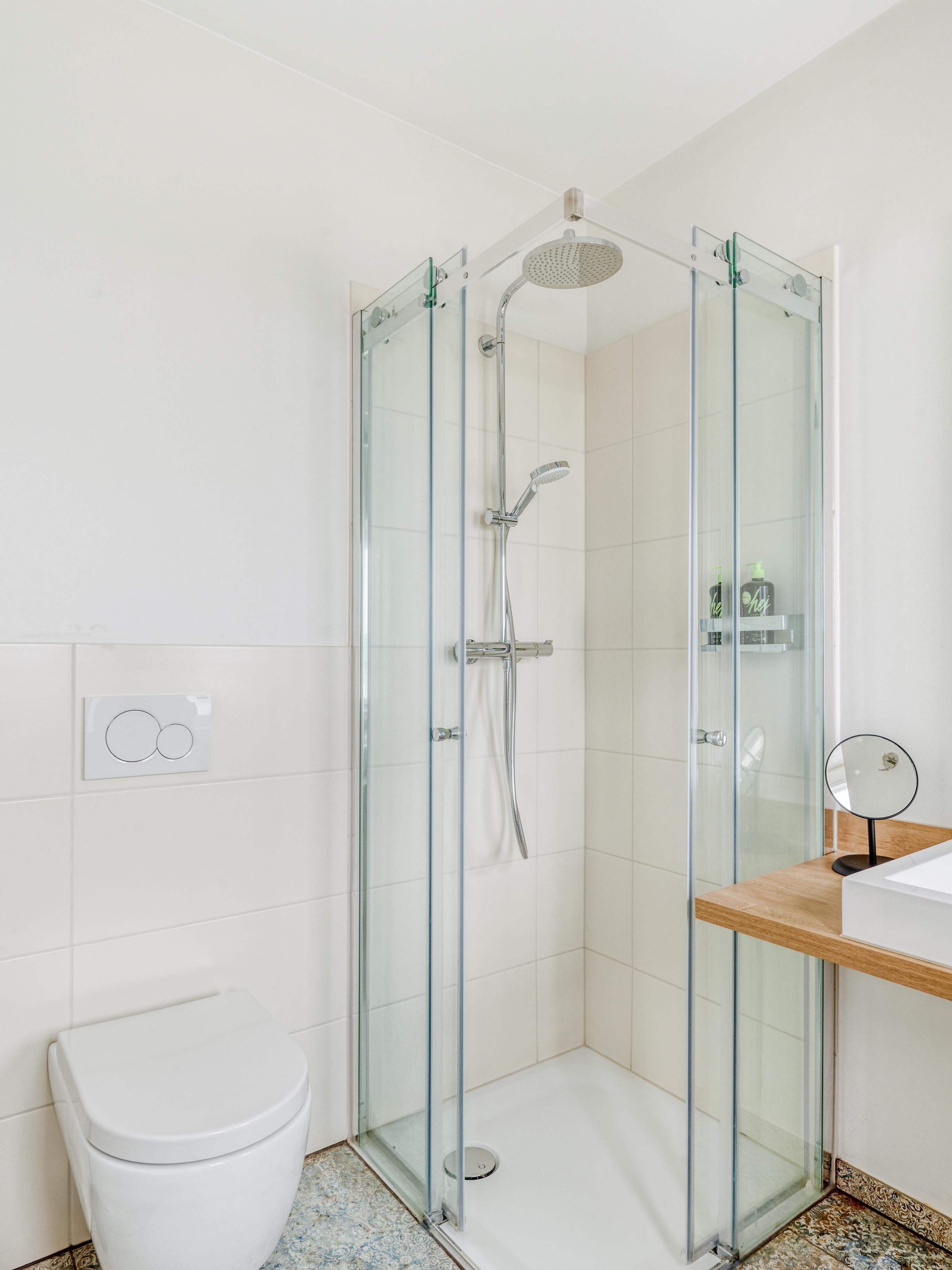 Un baño moderno con ducha envuelta en vidrio, inodoro blanco y tocador de madera con espejo.