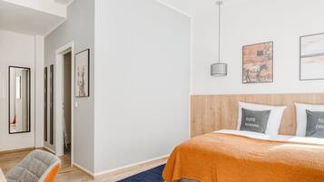 A modern bedroom with a bed, a wooden headboard, and a blue rug. There are framed pictures on the wall and a hanging light fixture.