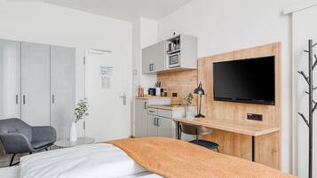 A modern junior room with a bed, a desk, a TV, and a kitchenette.