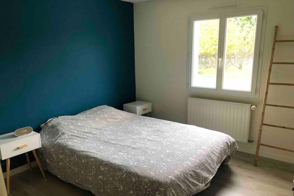 A bedroom with a bed, a nightstand, a window, and a radiator.