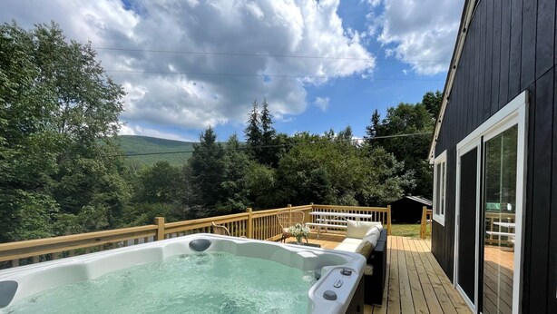 Un bain à remous sur une terrasse en bois, avec vue sur une zone boisée et des montagnes en arrière-plan.