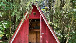 Une petite cabane en bois rouge, avec un toit triangulaire, une petite fenêtre et une porte.
