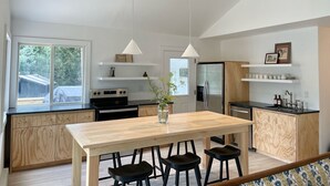 Une cuisine moderne avec une table en bois, des tabourets de bar noirs, un réfrigérateur en acier inoxydable et des luminaires suspendus.