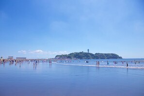 Una playa con gente, cielo despejado y una isla distante con una torre.