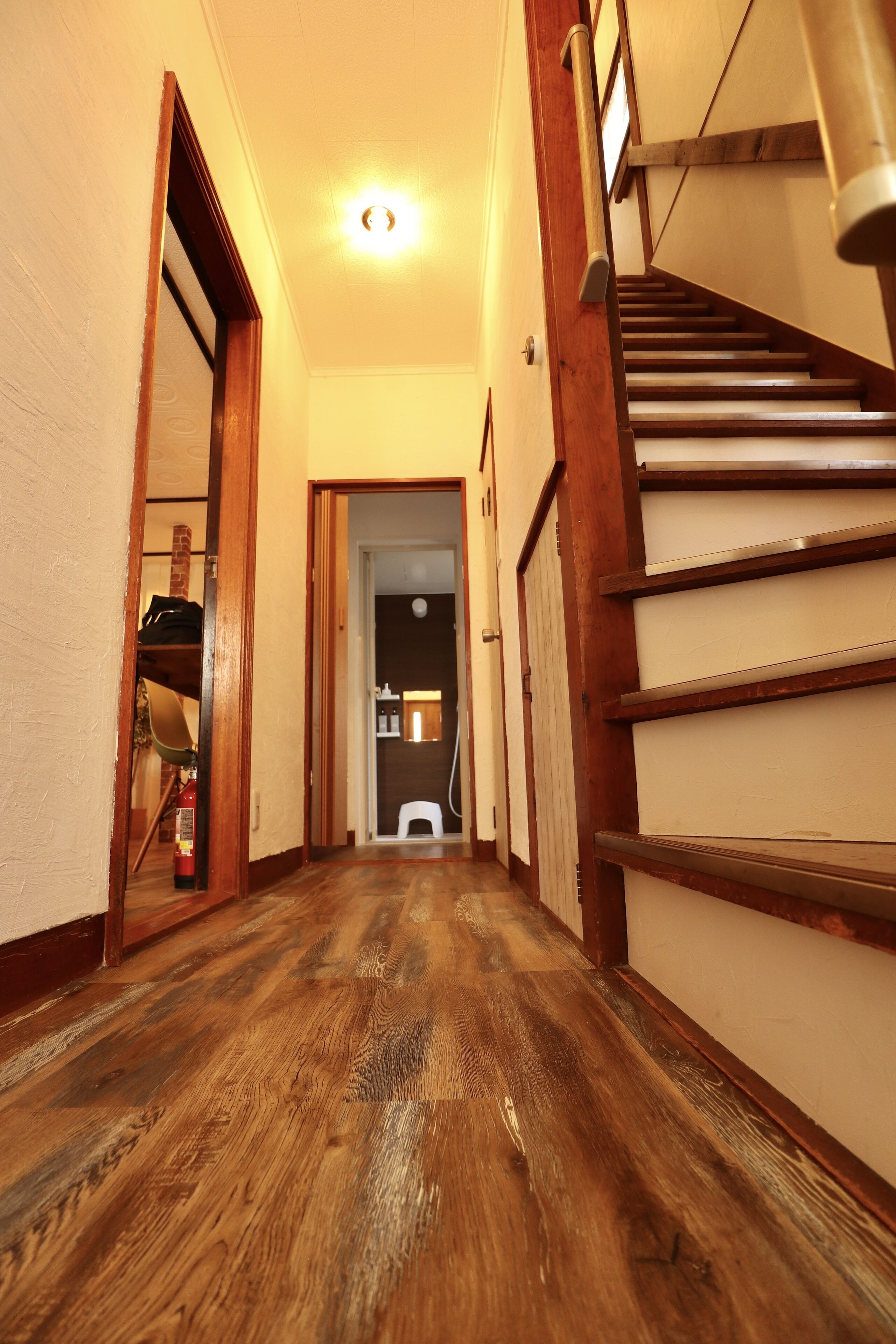 A narrow hallway with wooden flooring and a staircase on the right.