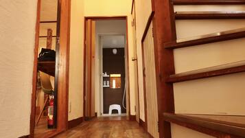 A narrow hallway with wooden flooring and a staircase on the right.