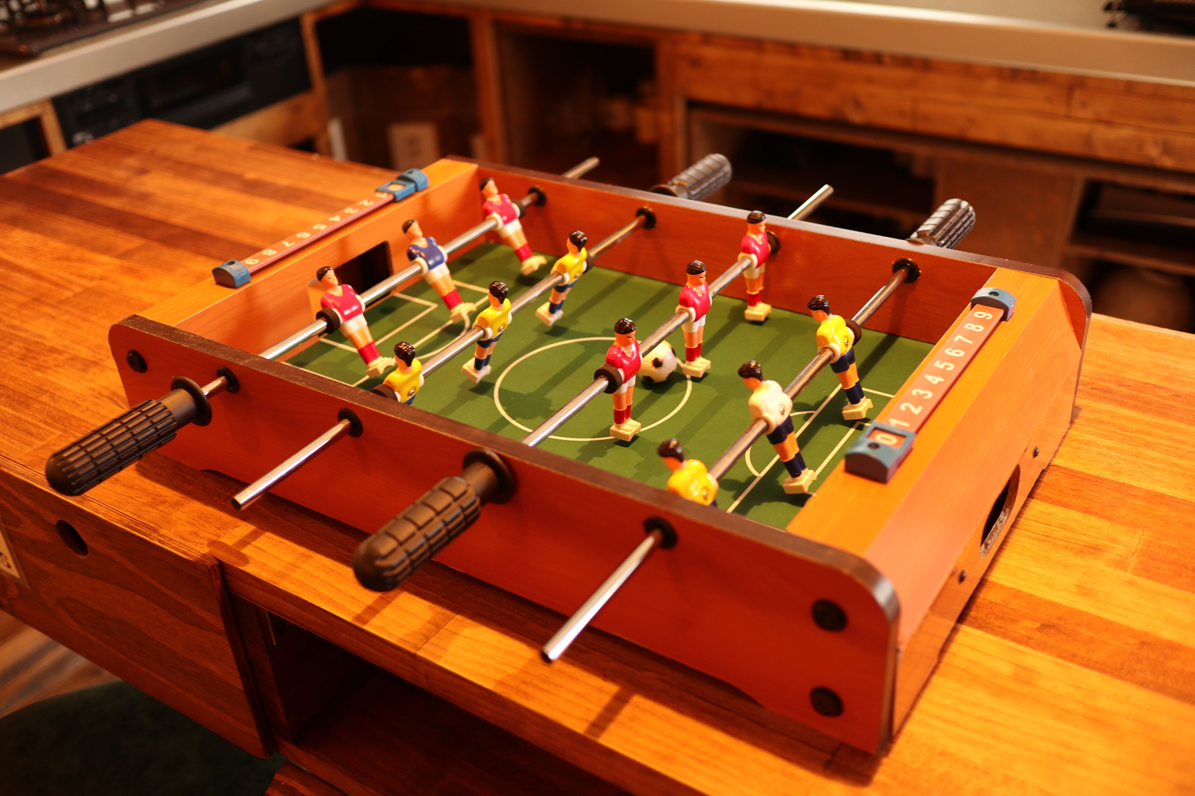 Una mesa de fútbol de madera con diseño de campo de fútbol, con figuras de jugadores en uniformes rojos y amarillos.