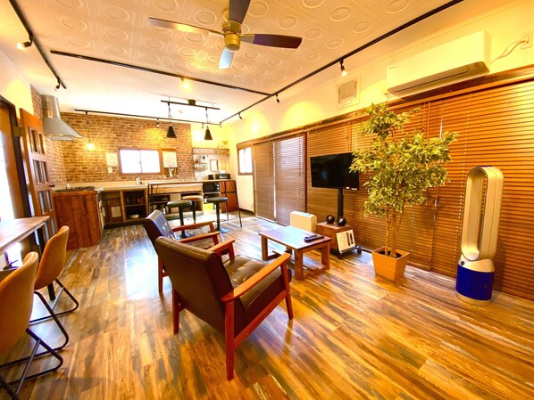 Una sala de estar moderna con suelo de madera, sillones de cuero, un televisor y una planta grande.