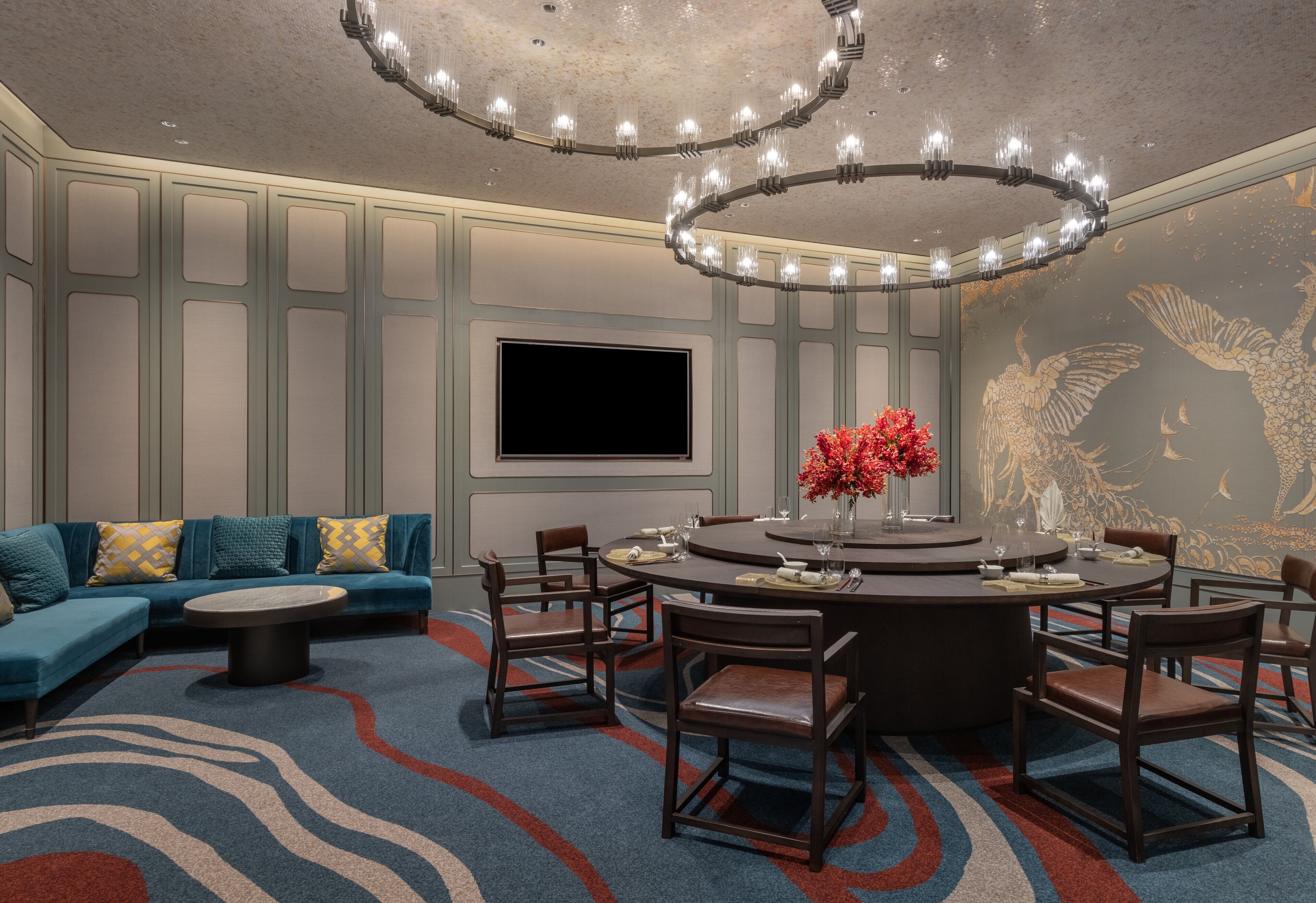 Une chambre d’hôtel moderne avec une table de salle à manger ronde, un canapé et un téléviseur fixé au mur.