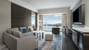 A modern hotel room with a sofa, a dining table, a kitchen area, and a large window offering a city view. - Crowne Plaza Xiamen Jimei by IHG (Xiamen)