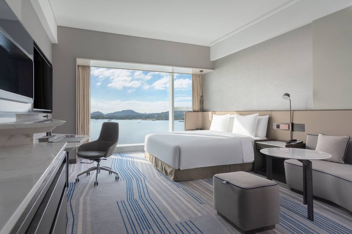 A modern hotel room with a large bed, a desk, a chair, a sofa, and a TV.