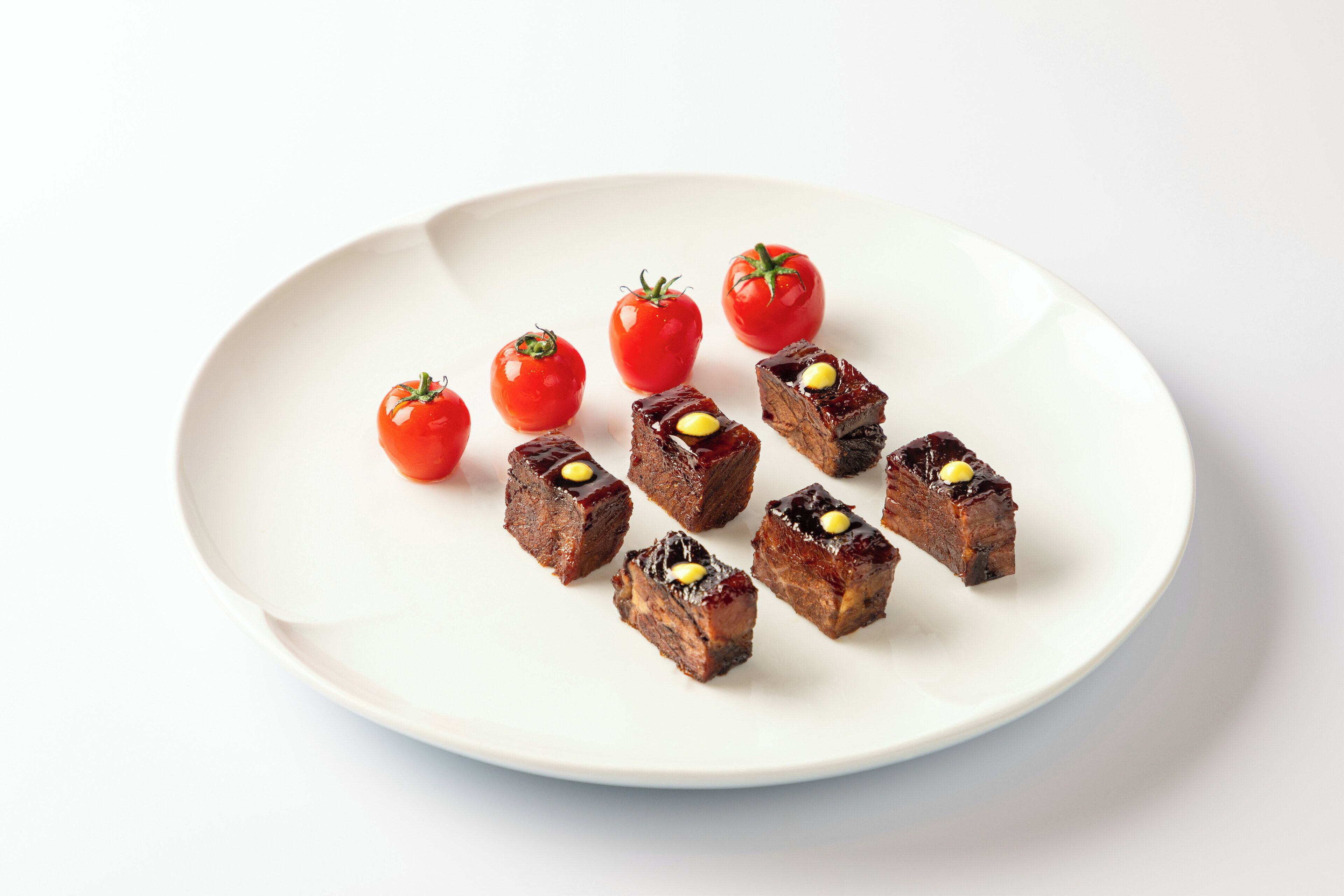 Een wit bord met kleine rode tomaten en bruine blokjes, vermoedelijk etenswaren.