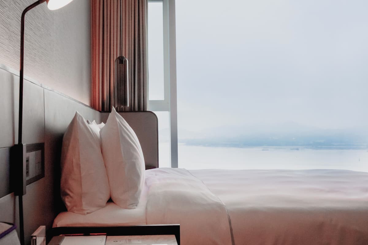 A hotel room with a bed, a bedside table, a lamp, and a view of the sea.