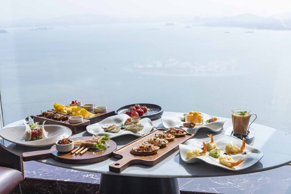 A table with various dishes and drinks, overlooking a body of water. - Crowne Plaza Xiamen Jimei by IHG (Xiamen)
