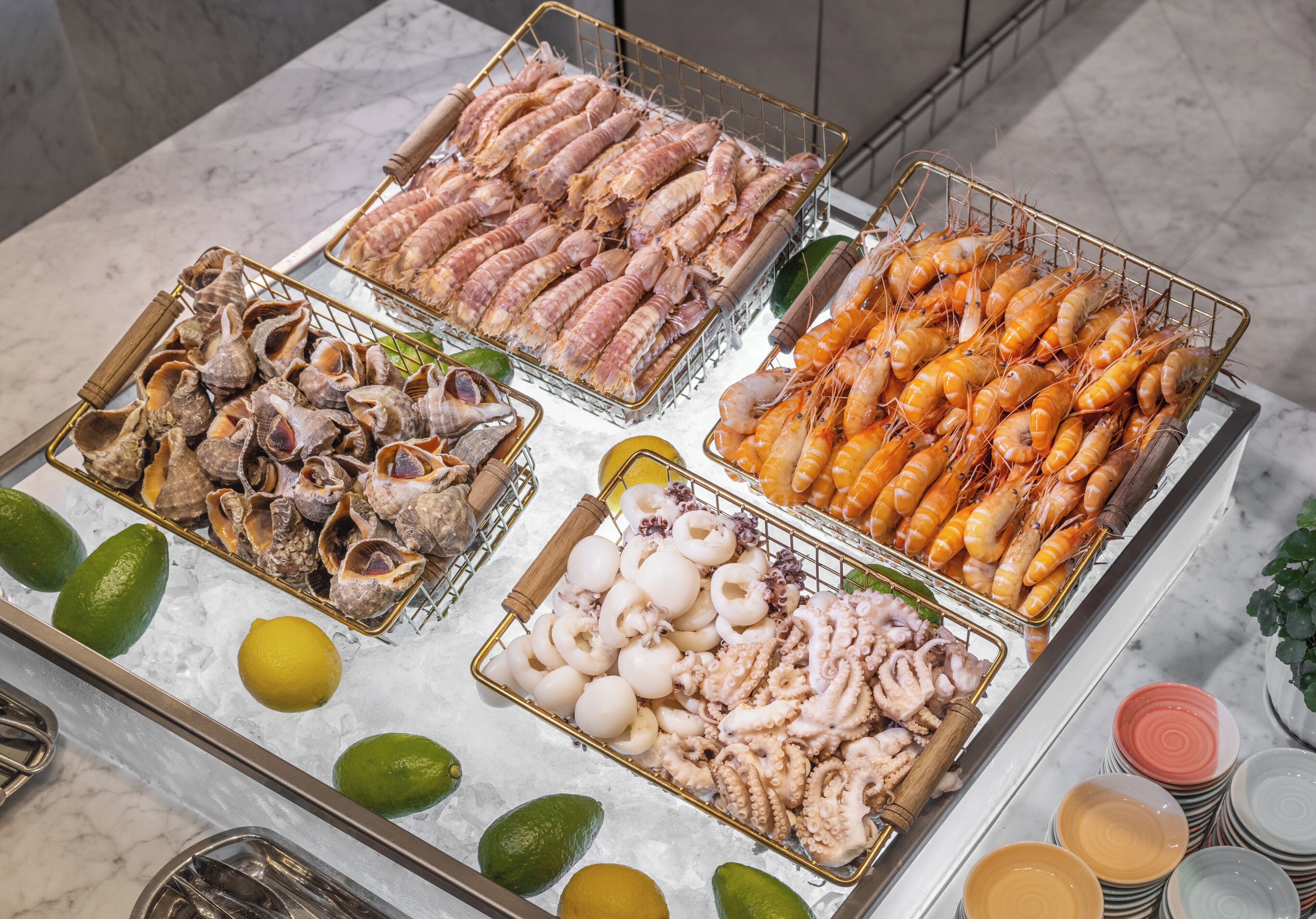 A seafood display with various types of shellfish and shrimp on ice, accompanied by lime wedges.
