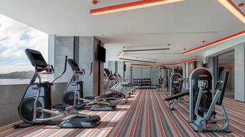 A modern gym with various exercise equipment, a patterned floor, and a large window offering a view of the outdoors.