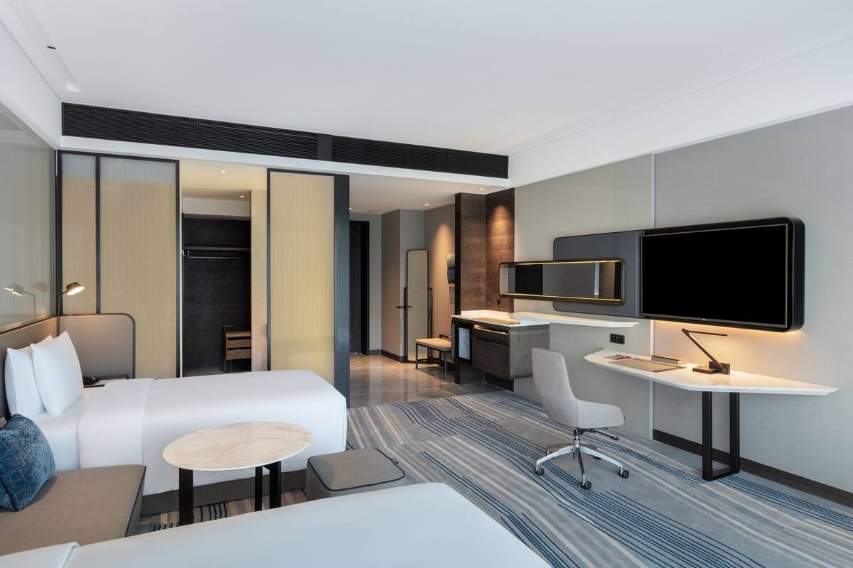 A modern hotel room with a large bed, a desk, a chair, a TV, and a walk-in closet.