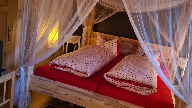 A wooden bed with a red mattress, white polka dot bedding, and a canopy.